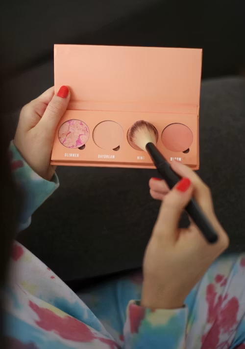 Person applying makeup with a brush on a peach eyeshadow palette